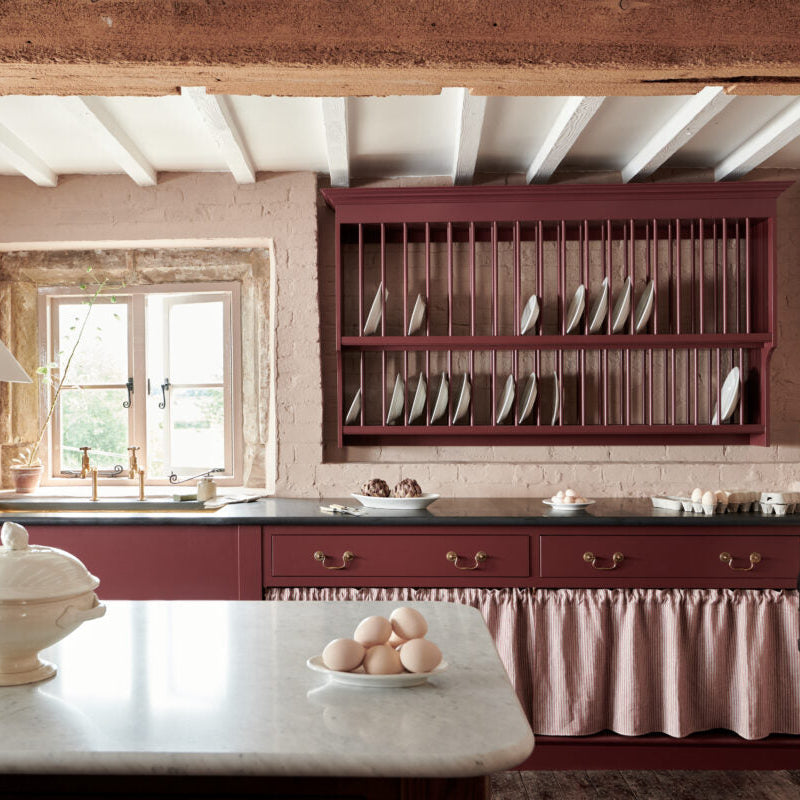 Kitchen with red cabinetry, marble island, and plate rack on brick wall.